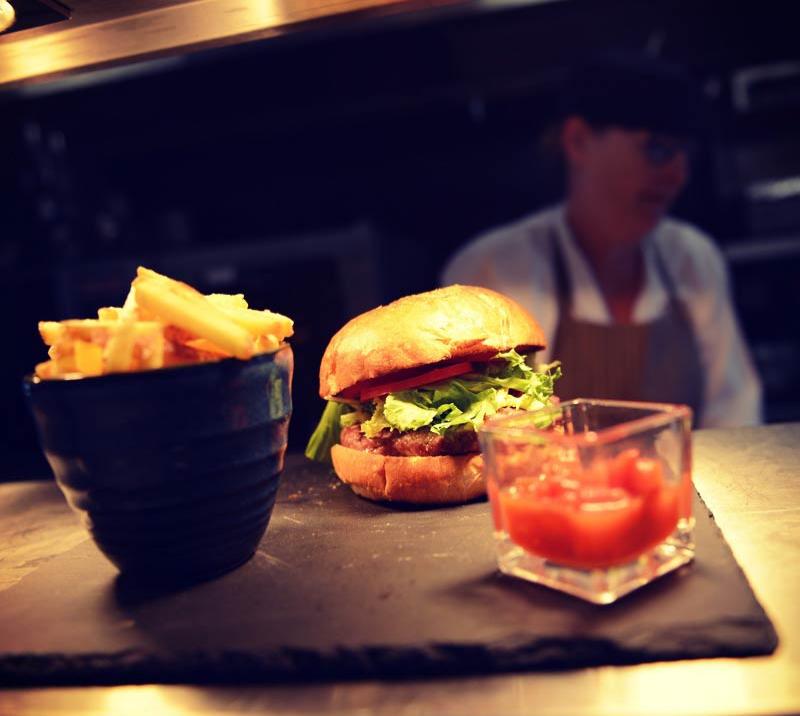 Close up of a gourmet burger and a cup full of chips set on a table.